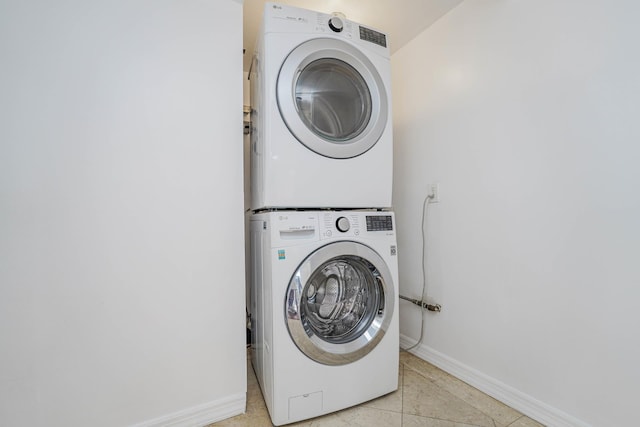 laundry area featuring light tile patterned floors, stacked washer / dryer, laundry area, and baseboards