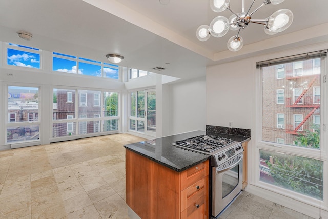 kitchen with visible vents, a notable chandelier, dark stone counters, brown cabinetry, and gas range