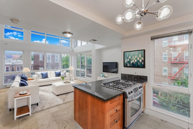 kitchen with brown cabinetry, visible vents, an inviting chandelier, dark stone counters, and stainless steel gas range oven