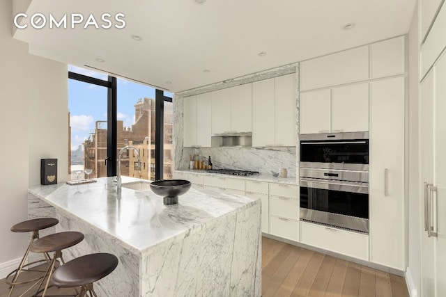 kitchen featuring stainless steel appliances, white cabinetry, tasteful backsplash, and light stone counters