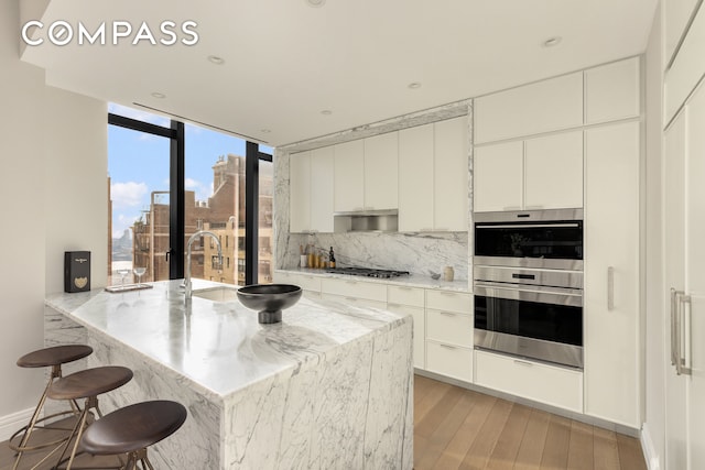 kitchen featuring backsplash, light stone countertops, a kitchen breakfast bar, light wood-style floors, and stainless steel appliances