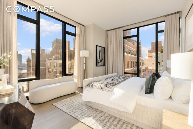 bedroom featuring access to outside, floor to ceiling windows, a city view, and wood finished floors