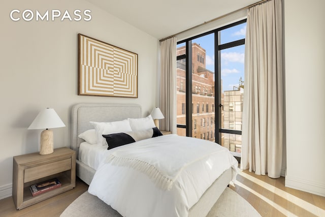 bedroom featuring expansive windows, access to outside, wood finished floors, and baseboards