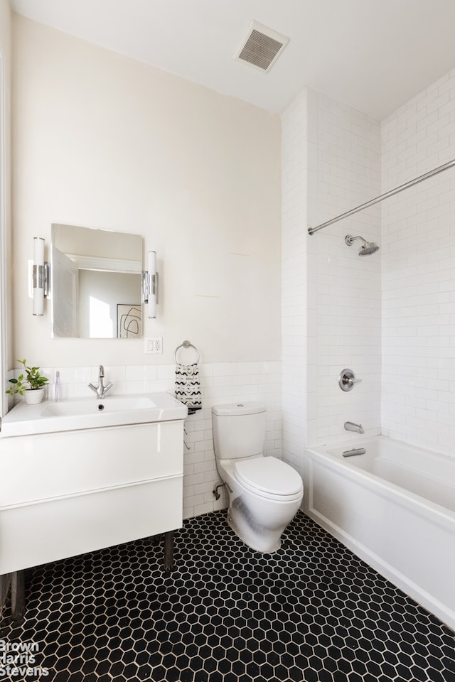 full bath featuring toilet, vanity, visible vents, tile walls, and shower / washtub combination