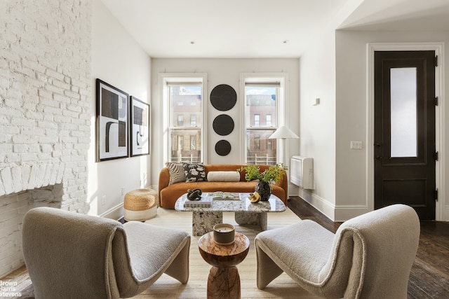 living area featuring a brick fireplace, baseboards, and wood finished floors