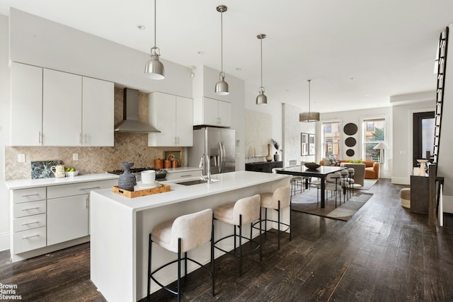 kitchen with a breakfast bar, a sink, stainless steel refrigerator with ice dispenser, wall chimney exhaust hood, and dark wood finished floors