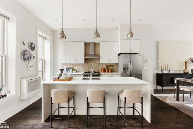 kitchen with wall chimney exhaust hood, appliances with stainless steel finishes, a breakfast bar, and backsplash