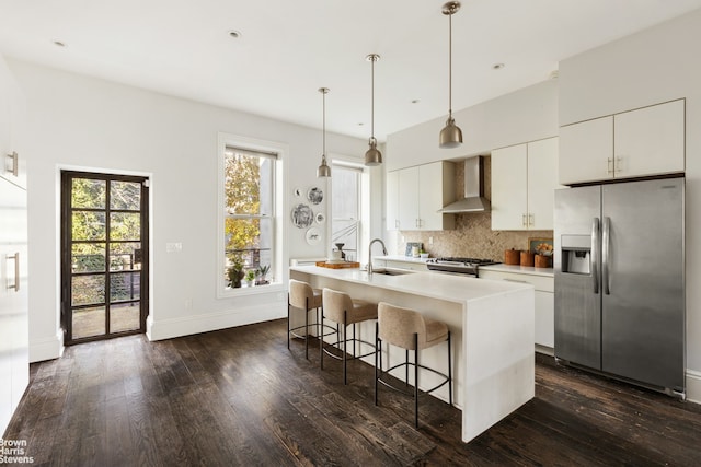 kitchen featuring a breakfast bar area, stainless steel appliances, decorative backsplash, a kitchen island with sink, and wall chimney range hood