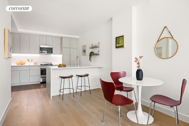 kitchen with a kitchen breakfast bar, light hardwood / wood-style floors, stainless steel appliances, kitchen peninsula, and gray cabinets