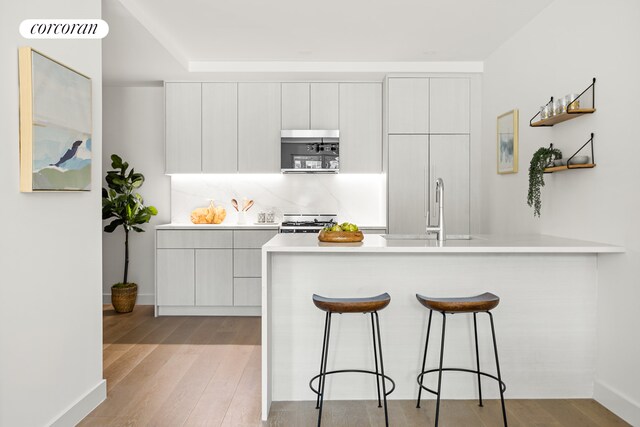 kitchen with white cabinetry, backsplash, light hardwood / wood-style flooring, and stove