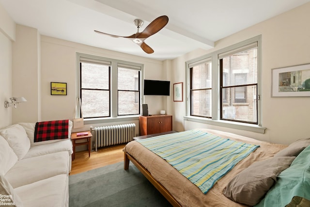 bedroom featuring a ceiling fan, radiator, beam ceiling, and wood finished floors