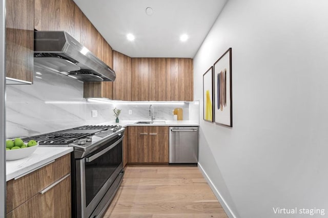 kitchen with appliances with stainless steel finishes, sink, decorative backsplash, and light wood-type flooring