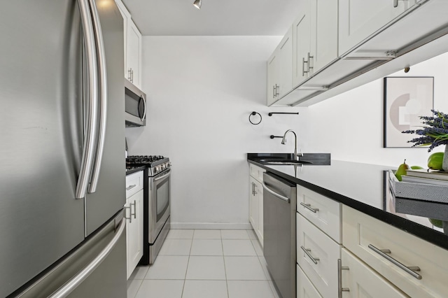 kitchen with light tile patterned flooring, stainless steel appliances, a sink, white cabinets, and dark countertops