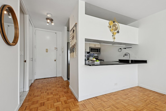 kitchen featuring stainless steel microwave, dark countertops, baseboards, and a sink