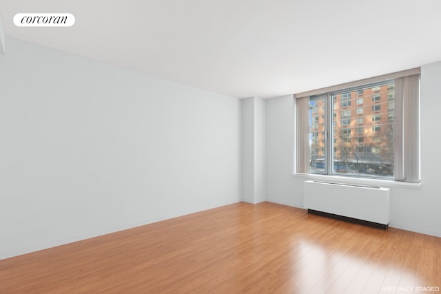 unfurnished room featuring light wood-style floors, radiator, visible vents, and baseboards