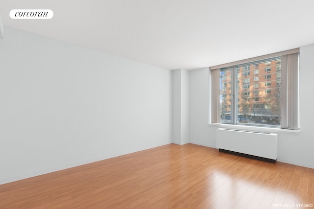 empty room with light wood finished floors, visible vents, radiator heating unit, and baseboards