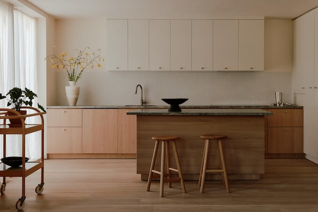 kitchen featuring light wood-type flooring, modern cabinets, a sink, a kitchen breakfast bar, and decorative backsplash