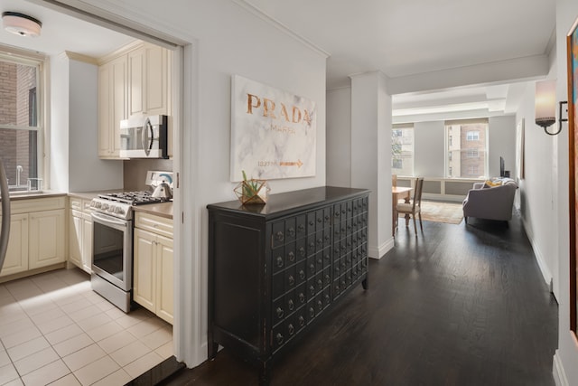 kitchen with crown molding, light wood-style flooring, cream cabinets, mail area, and appliances with stainless steel finishes