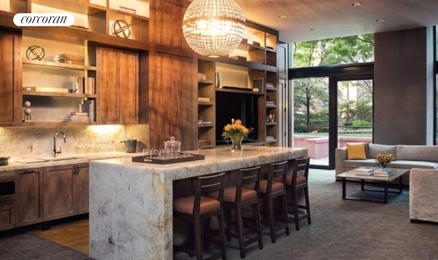 200 E 94th St Unit 1012, New York City, NY 10128 - kitchen featuring open shelves, a breakfast bar area, a chandelier, light stone counters, and a kitchen island