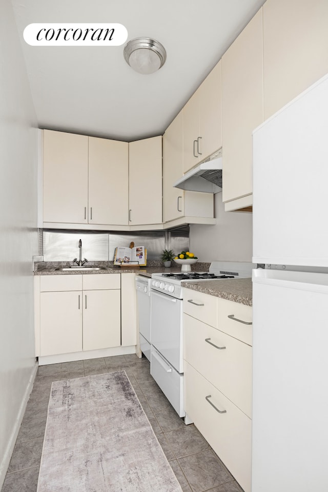 kitchen with light tile patterned floors, cream cabinets, a sink, white appliances, and under cabinet range hood