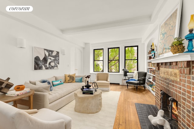 living room featuring beam ceiling, visible vents, light wood-style flooring, and a brick fireplace