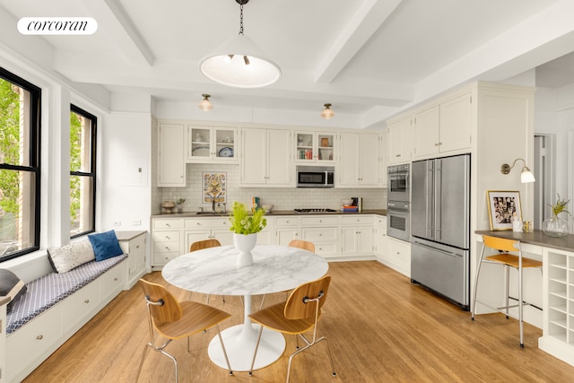 kitchen with stainless steel appliances, visible vents, backsplash, light wood-style flooring, and beamed ceiling