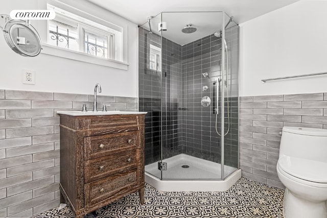 bathroom with toilet, a shower with shower door, tile walls, vanity, and tile patterned flooring