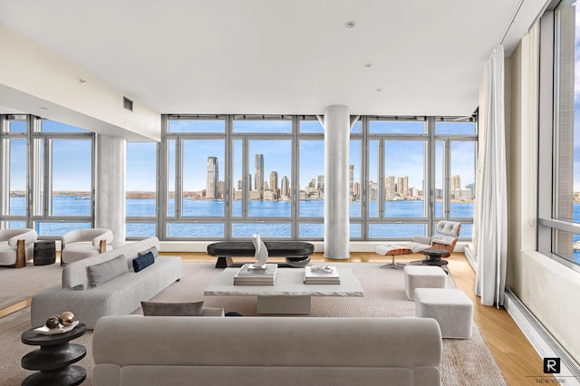 living area featuring a view of skyline, light wood-type flooring, a water view, and floor to ceiling windows
