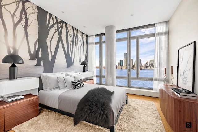 bedroom with a water view, light wood-type flooring, floor to ceiling windows, access to exterior, and a view of skyline