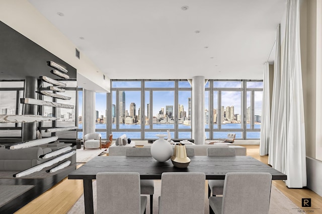 dining space with expansive windows, light wood-type flooring, a view of city, and visible vents