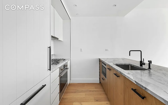 kitchen featuring sink, appliances with stainless steel finishes, light stone countertops, light hardwood / wood-style floors, and white cabinets