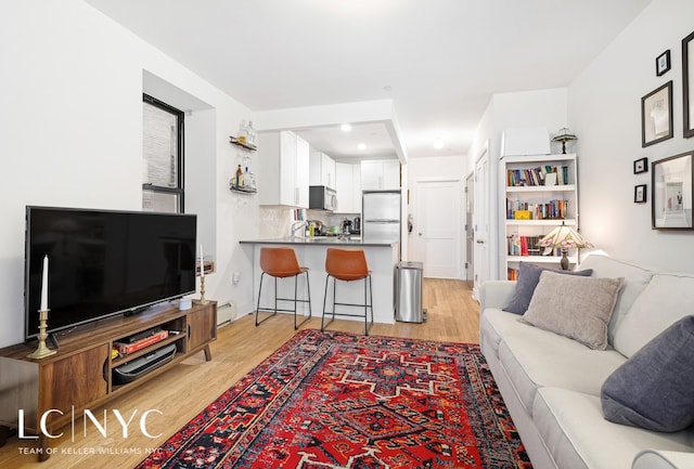 living room featuring baseboard heating, sink, and light hardwood / wood-style flooring