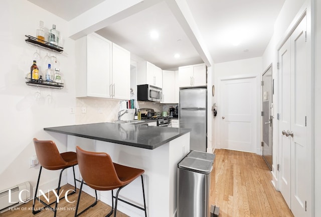 kitchen featuring a baseboard radiator, stainless steel appliances, a peninsula, a sink, and a kitchen breakfast bar