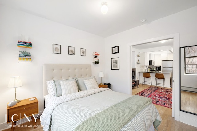 bedroom with light wood finished floors, a baseboard radiator, and refrigerator