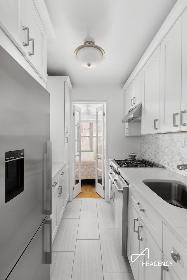 kitchen featuring stainless steel appliances, decorative backsplash, white cabinets, a sink, and under cabinet range hood