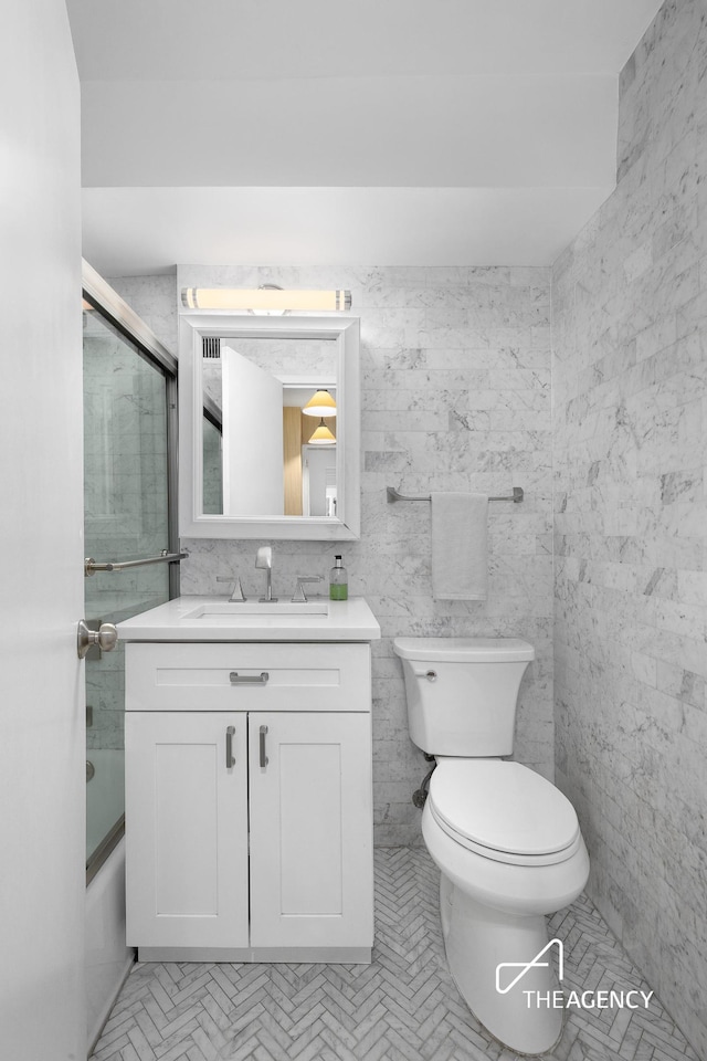 bathroom with combined bath / shower with glass door, vanity, toilet, and tile walls