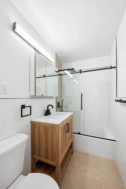 full bathroom with tile walls, bath / shower combo with glass door, vanity, tile patterned floors, and toilet