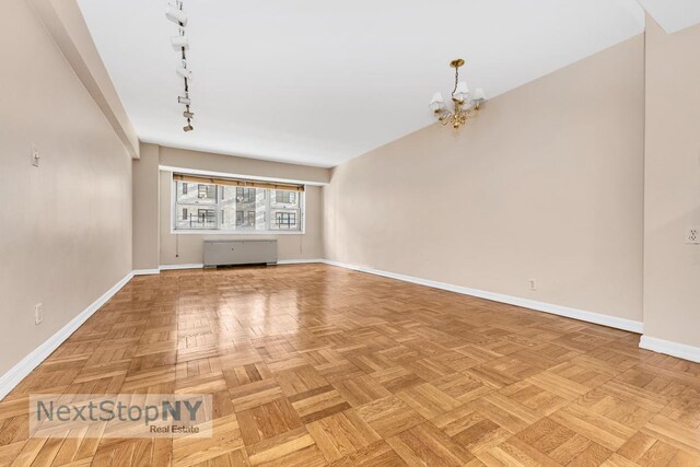 unfurnished living room featuring a notable chandelier, track lighting, and light parquet flooring