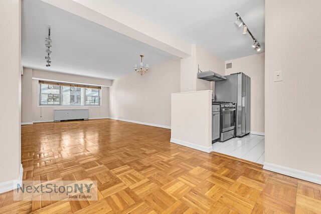 unfurnished living room with track lighting, a chandelier, and light parquet floors