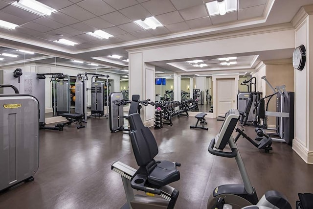 gym with a paneled ceiling, ornamental molding, and a raised ceiling