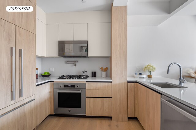 kitchen featuring light brown cabinetry, white cabinetry, sink, light hardwood / wood-style floors, and stainless steel appliances