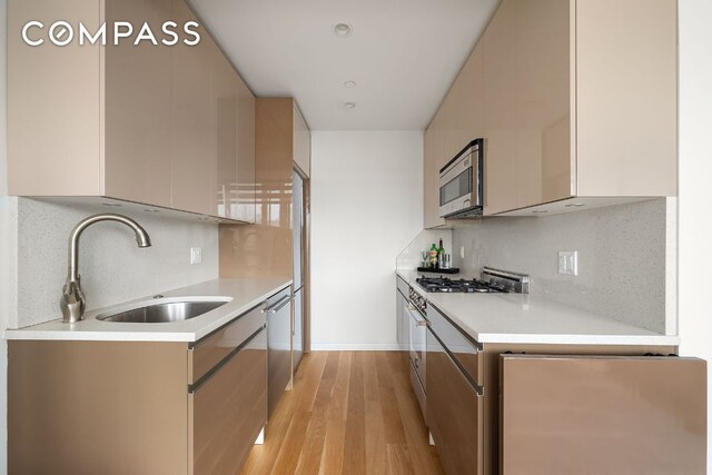 kitchen with appliances with stainless steel finishes, sink, decorative backsplash, and light hardwood / wood-style flooring