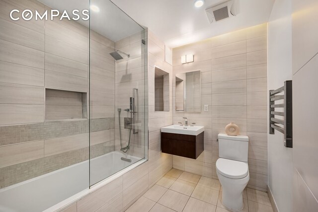 full bathroom featuring tile walls, tile patterned flooring, tiled shower / bath combo, vanity, and toilet