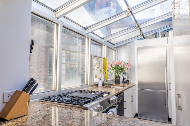 kitchen featuring stone countertops, a sink, white cabinetry, stainless steel built in fridge, and gas stove