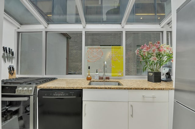 kitchen featuring appliances with stainless steel finishes, white cabinets, a sink, and light stone countertops