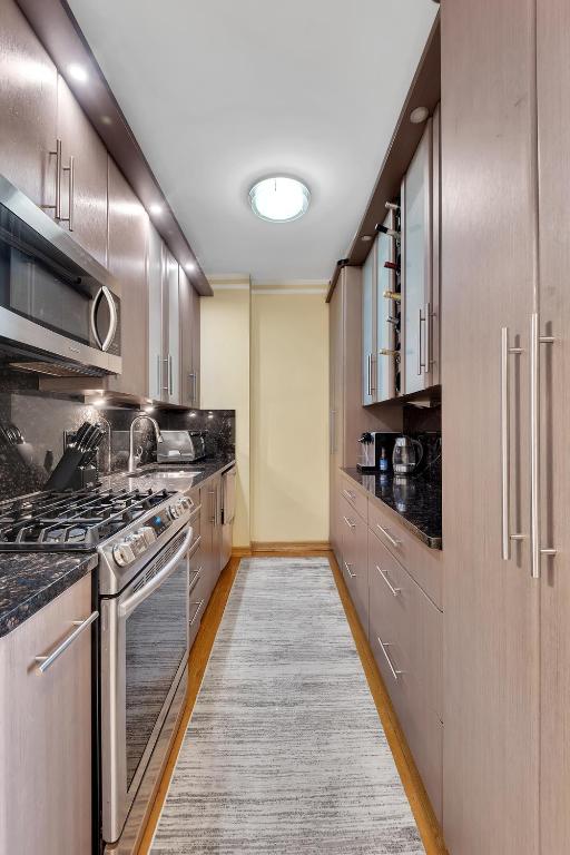 kitchen featuring light wood-style flooring, dark stone countertops, a sink, stainless steel appliances, and backsplash