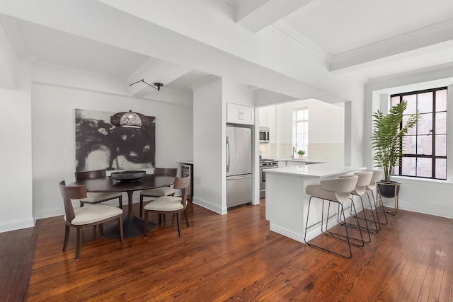 kitchen with beamed ceiling, dark wood-type flooring, appliances with stainless steel finishes, a breakfast bar area, and a peninsula