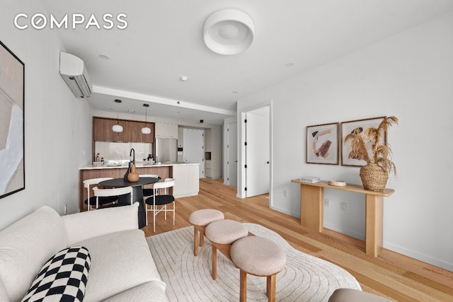 living area with light wood finished floors, baseboards, and a wall mounted air conditioner