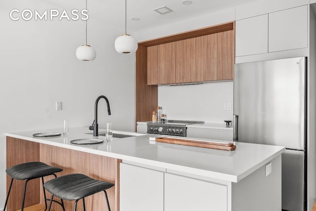 kitchen featuring decorative light fixtures, light countertops, freestanding refrigerator, white cabinets, and a sink