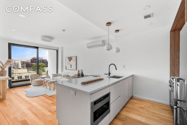 kitchen with light wood finished floors, stainless steel microwave, a sink, and a wall mounted AC